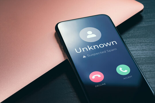 Spam call warning on smartphone screen with unknown caller and suspected scam alert beside laptop. Scam phone mobile fraud, robocall protection and spam cell call cybersecurity concept