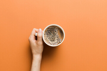 Obraz premium Minimalistic style woman hand holding a cup of coffee on Colored background. Flat lay, top view cappuccino cup. Empty place for text, copy space. Coffee addiction. Top view, flat lay