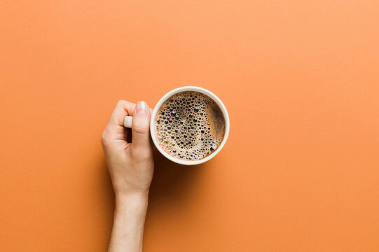 Minimalistic style woman hand holding a cup of coffee on Colored background. Flat lay, top view cappuccino cup. Empty place for text, copy space. Coffee addiction. Top view, flat lay