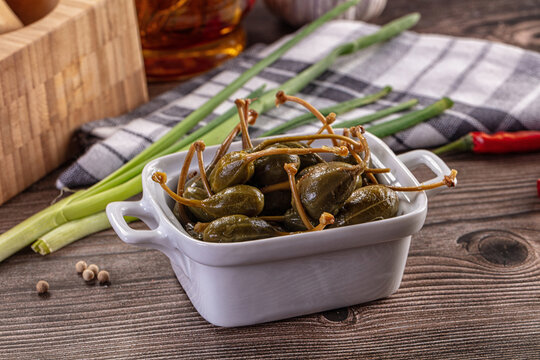 Pickled caper berries in a bowl with fresh ingredients on a rustic wooden table.