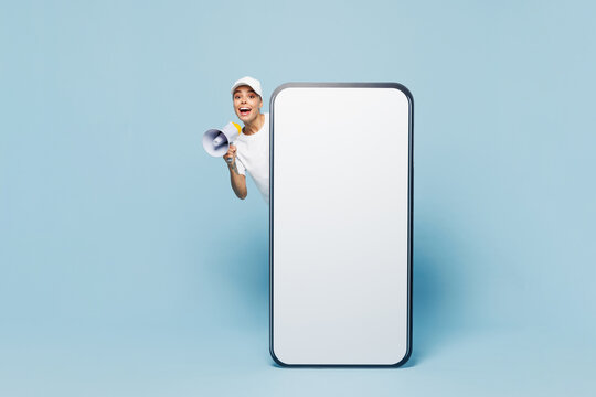 Full length delivery employee woman wear white cap T-shirt uniform work as dealer courier stand at big blank screen mobile cell phone with workspace isolated on plain blue background. Service concept.