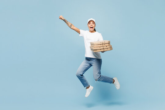 Full body delivery employee woman wear white cap T-shirt uniform workwear work as dealer courier hold pizza in cardboard flatbox jump isolated on plain pastel blue background studio. Service concept.