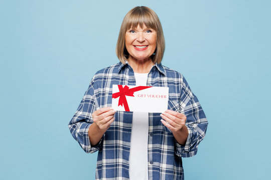 Elderly happy blonde woman 50s years old wear checkered shirt casual clothes hold certificate coupon voucher card for store isolated on plain pastel light blue background studio Lifestyle concept