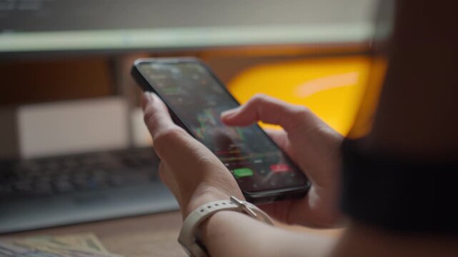 Person using smartphone with stock market charts on screen. Trader analyzing financial data on trading app. Concept of online trading, investment analysis and financial risk