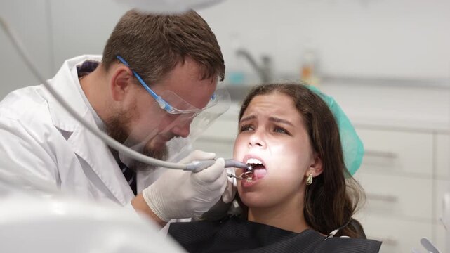 Qualified male dentist carefully drills into a woman tooth to remove caries and make a filling. Woman undergoing treatment in a dental clinic. High quality 4k footage