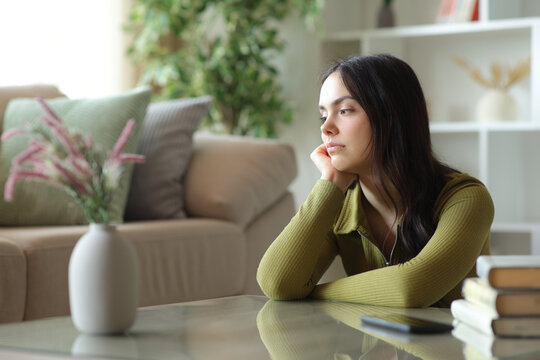 Sad pensive young woman looking down at home