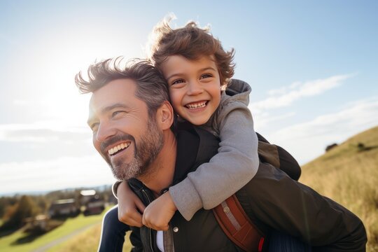Happy father giving piggyback ride to his cheerful son with sun flare