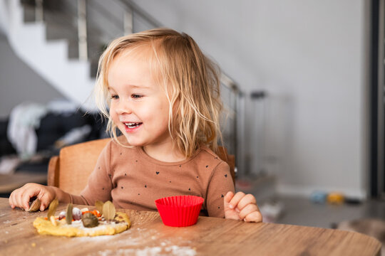 Happy toddler girl playing with dough at a wooden table