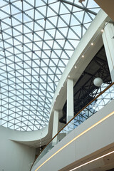 Fototapeta premium Vertical shot of modern commercial atrium featuring geometric glass roof, curved balcony, copy space, presenting contemporary architecture for corporate branding, real estate marketing