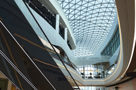 Wide angle view of modern commercial atrium featuring escalators, glass roof, curved architecture, supporting retail, office, or corporate real estate marketing and leasing