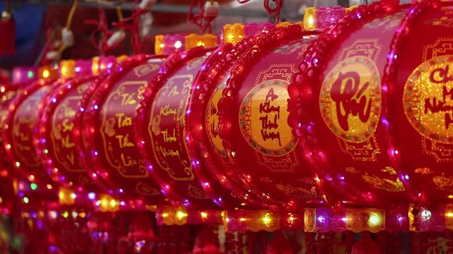 Traditional Vietnamese Tet holiday decoration close up. Red glowing lanterns with golden calligraphy text and lights at a festive street market during Lunar New Year in Nha Trang, Khanh Hoa, Vietnam.
