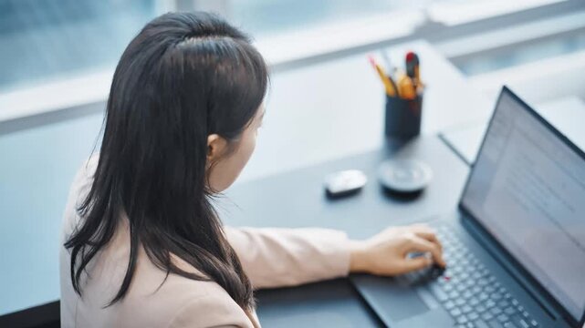 Young Asian Businesswoman Working on Laptop in Modern Office. Professional Female Employee Typing on Computer Keyboard at Desk, Focused on Work and Productivity.