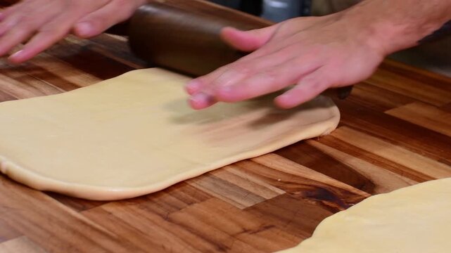 Man rolling dough with wooden pin on table, focused kitchen scene