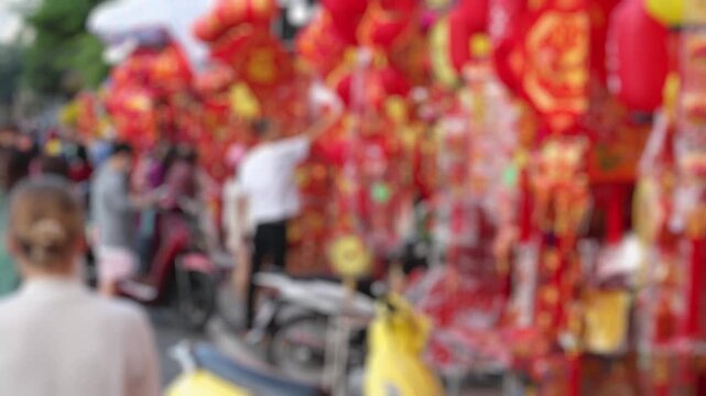 Bokeh view of Vietnamese people buying traditional red lanterns and lucky ornaments at a festive street market before Tet holiday. Lunar New Year shopping concept. Blurred background footage.