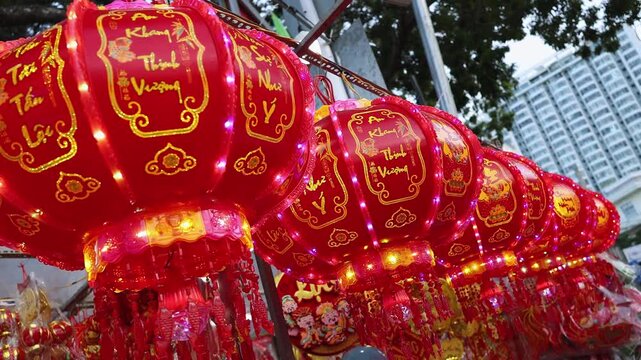Traditional Vietnamese Tet holiday decoration close up. Red glowing lanterns with golden calligraphy text and lights at a festive street market during Lunar New Year in Nha Trang, Khanh Hoa, Vietnam.