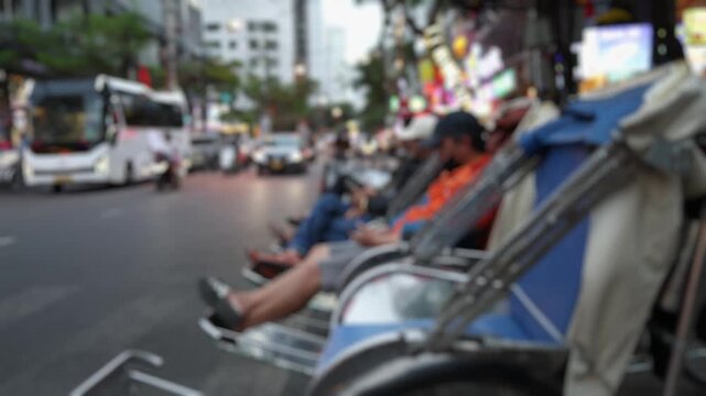 Bokeh view of Vietnamese cyclo drivers waiting for passengers on a street in Nha Trang, Vietnam. Close-up of traditional cycle rickshaw riders resting on their vehicles.  Blurred background footage.