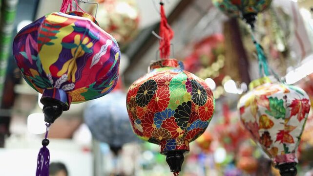 Traditional souvenir lanterns for sale at a Vietnamese street shop in Vietnam. Close-up of colorful oriental fabric lanterns with floral patterns hanging at a local market. Asian cultural footage.