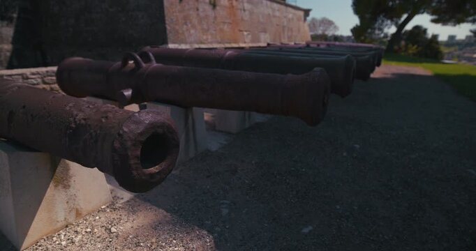 Row of cannons on the grounds of Pula Castle beside a stone fortress wall.