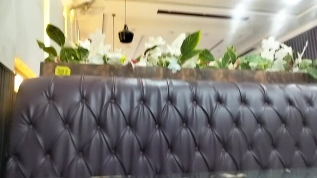Elegant tufted leather sofa in a modern restaurant interior with decorative green plants and hanging ceiling lights in motion