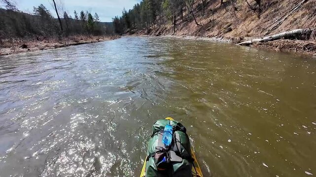 Sunlit river surface with glinting waves, bright glare dances across fastmoving water, rocky banks and pine slopes, brisk downstream speed, reflective shimmer and energetic motion.