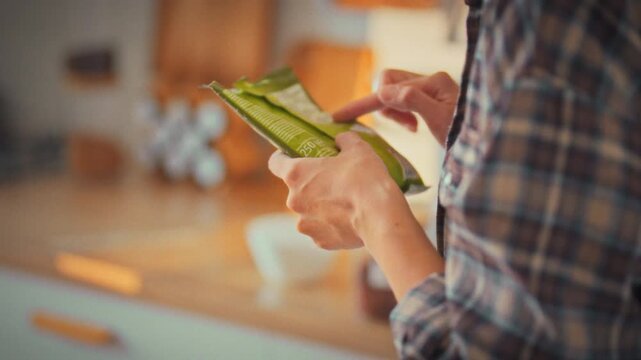 In a bright home kitchen, a young woman meticulously examines the label on a soft package, ensuring informed choices about nutrition and healthcare through careful product composition analysis