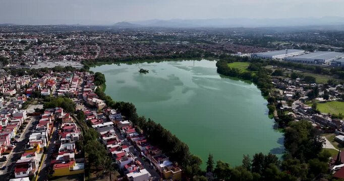 Drone flight above suburban neighborhoods north of Mexico City, featuring Axotl&aacute;n Lagoon in the foreground. Urban expansion and natural water landscapes define the metropolitan scenery.