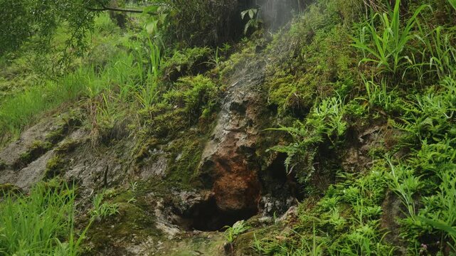 A detailed shot of an active volcanic vent emitting sulfuric steam on a lush green hillside.