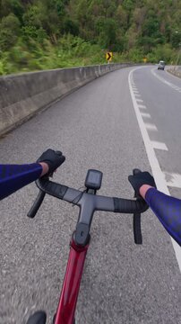 View from a cyclist's perspective on a winding mountain road, showcasing handlebars, a bike computer, and lush greenery.