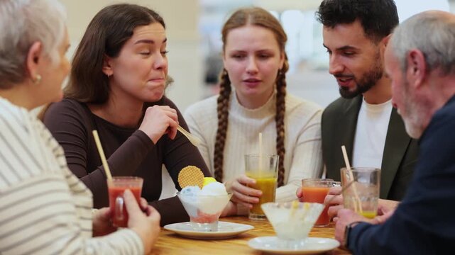 Large friendly family gathered at table to have meeting in restaurant or cafe. Relatives drink juice or coffee, and socialize. People participate in discussion during meeting