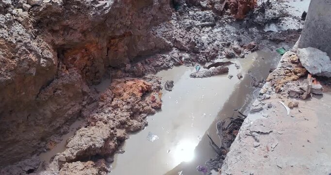 Close up of an excavator bucket digging into wet, muddy earth within a trench at a construction site