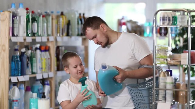 Family schoolboy son and dad are choosing liquid detergent in store. Customer reads label, compare varieties items. Deal and shopping in household store, choosing goods, inspect assortment