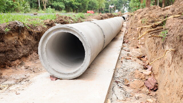 Concrete drainage pipe on the side of the road.  Close-up of long rows of concrete pipes in a trench on a cement foundation during construction of a sewerage system with selective focus.