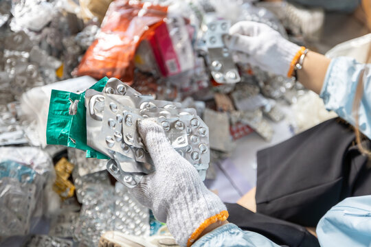 Gloved hand holding empty aluminum blister packs over a cardboard box for medical waste recycling and proper disposal.