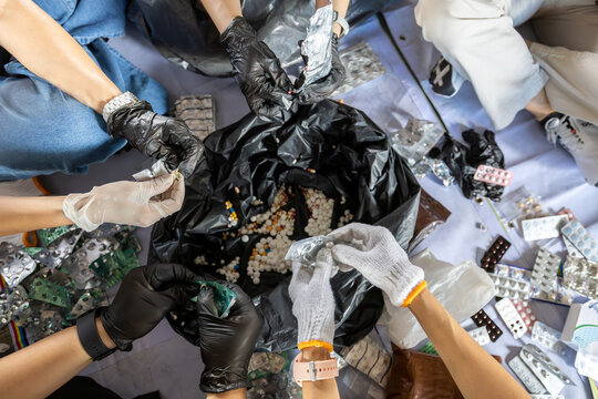 Top view of people wearing gloves sorting expired medication and empty blister packs for medical waste disposal and recycling.