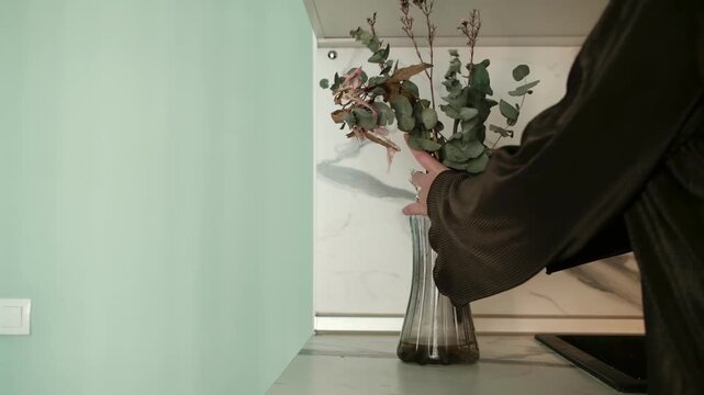 Woman taking dried flowers out of glass vase and placing them on table indoors. Home cleaning and wilted bouquet concept.