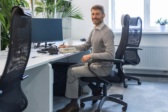 Handsome smiling employee, young entrepreneur looking at camera while sitting in the office