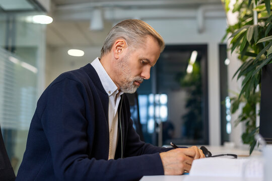 Portrait of adult businessman sitting at his desk in the office and making notes.