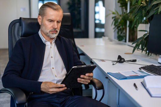 Smiling handsome mature businessman manager sitting in office with tablet computer