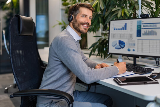 Happy man call center agent operator wearing headset in office, looking to camera working in customer support