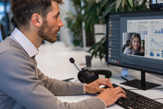 Happy smiling employee, young entrepreneur working on PC computer technology looking at camera working in office sitting at desk