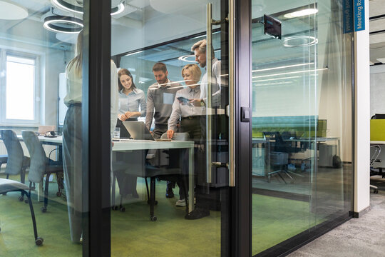 A modern office interior, featuring a blurred view of workers at desks, through a glass partition.