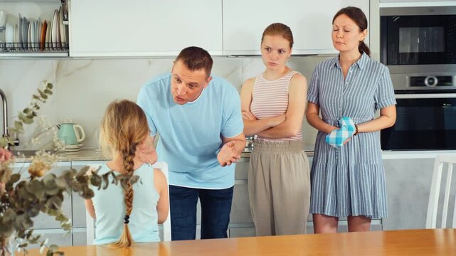 At home kitchen, parents scold daughter for careless act. Sulky preschool girl stand near table during serious conversation with parents
