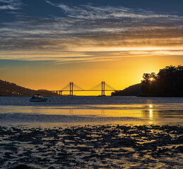 Obraz premium Golden hour seascape with anchored boat and suspension bridge