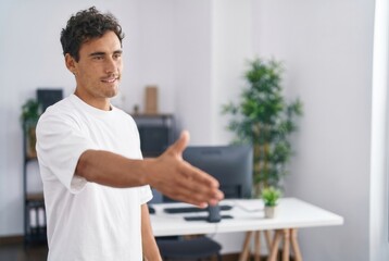 Fototapeta premium Young man extending his open hand forward, offering a handshake in a workspace