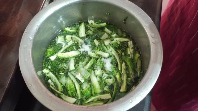 Mixing salt into chopped bitter gourd slices soaked in water with hands, reducing bitterness of green karela