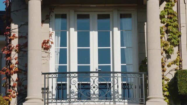 Panning camera revealing centered 2nd-floor balcony and French doors for detail, sunlight shifting