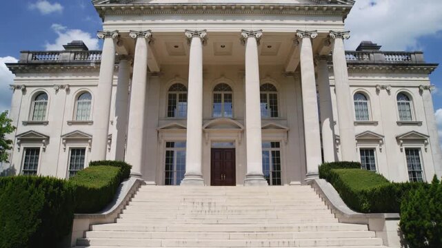 Moving camera filming neoclassical mansion facade on lawn showing columns, steps, doors