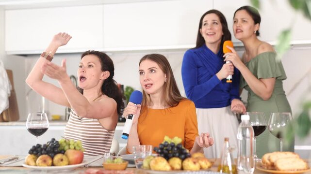 Group of women friends are having fun singing karaoke during feast and gatherings. With microphones in their hands, fans of modern music perform modern hits in fun home environment