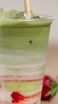 Process of making a strawberry matcha latte with fresh mashed berries. Ingredients of strawberry matcha in a plastic cup, mixed with a straw.