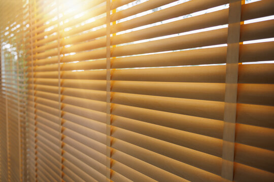Warm sunlight filters through horizontal window blinds, casting soft shadows and golden patterns across an interior space, symbolizing comfort, privacy, and modern home living atmosphere.
